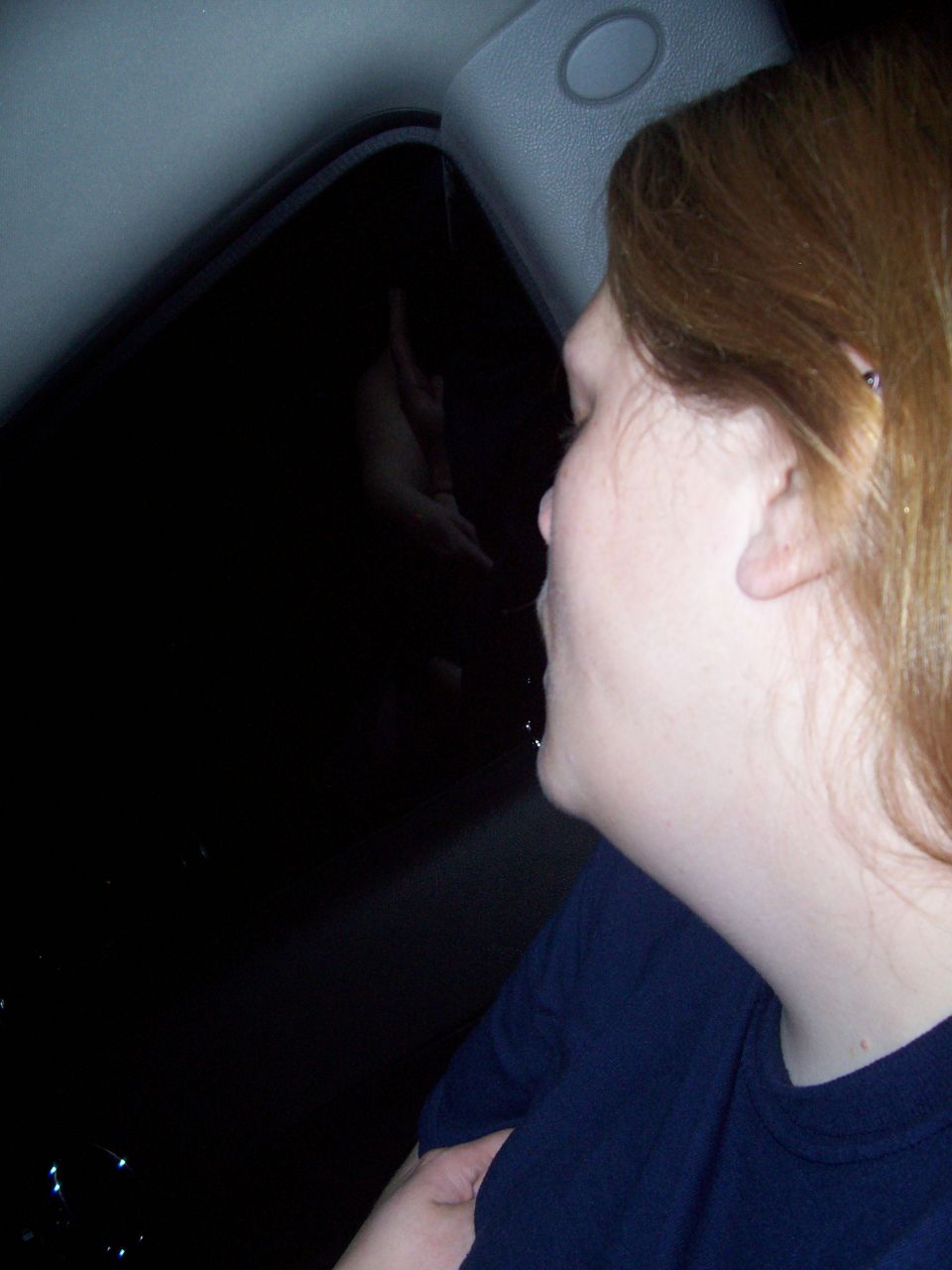 Woman looking out a dark car window at night, reflection visible in window