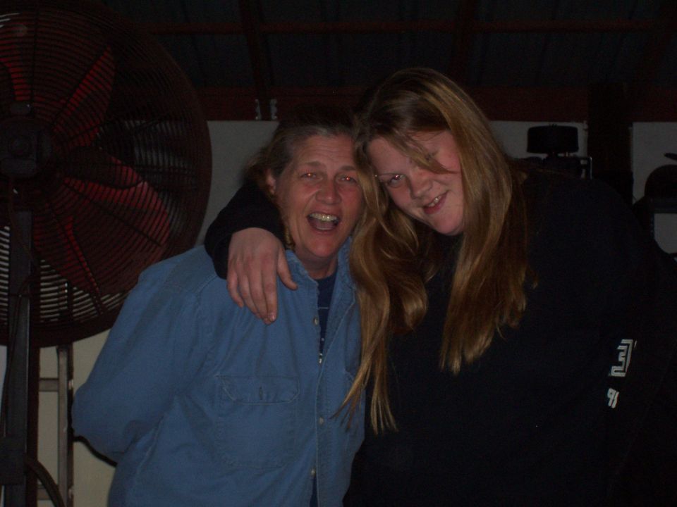 Two women pose for a photo in front of a large industrial fan