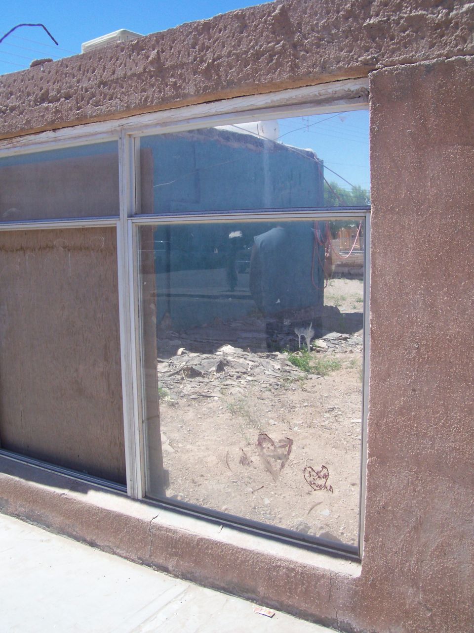 Reflection in a window shows a building and some debris. Two hearts are drawn on the glass