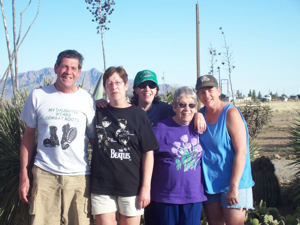 Group of five people posing in a desert yard with mountains behind