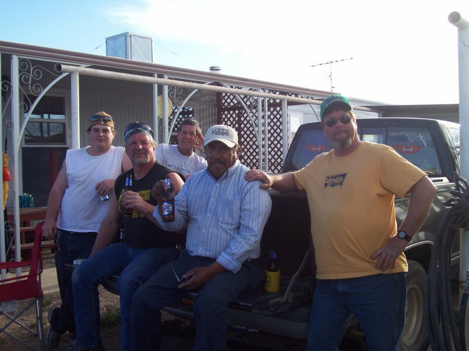 Five men holding beers posed against a dark pickup truck outdoors