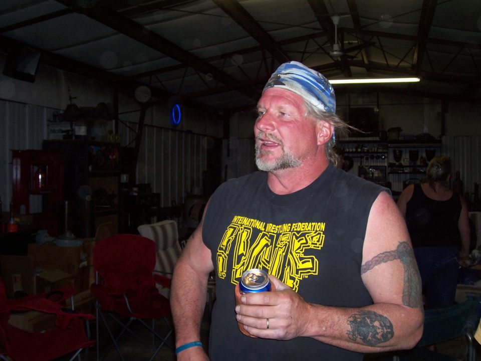 Man in black IWF wrestling tank top and bandana holding a can