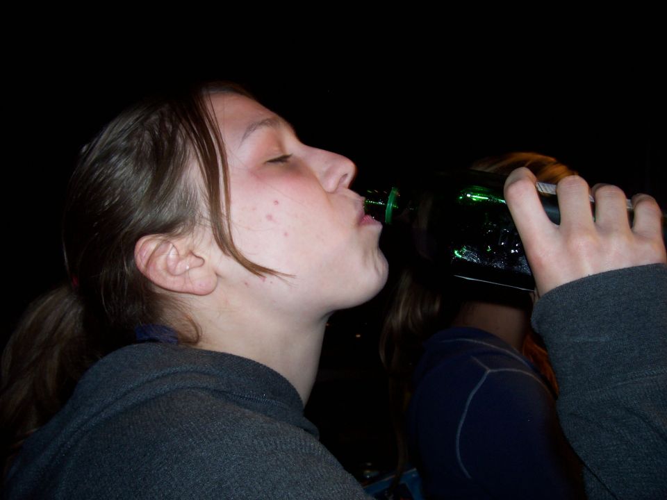 Young woman drinking from a green glass bottle at night