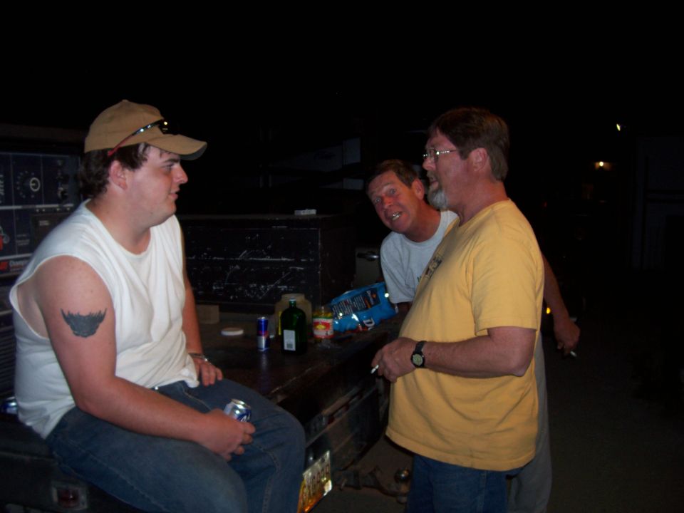 Three guys hanging out at night, one sitting on the tailgate of a truck