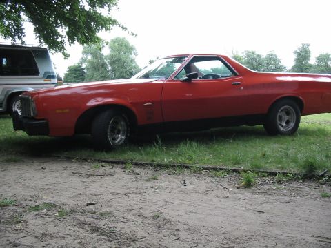 1974 Ford Ranchero - A red coupe utility vehicle is parked outdoors next to a white van under a tree.