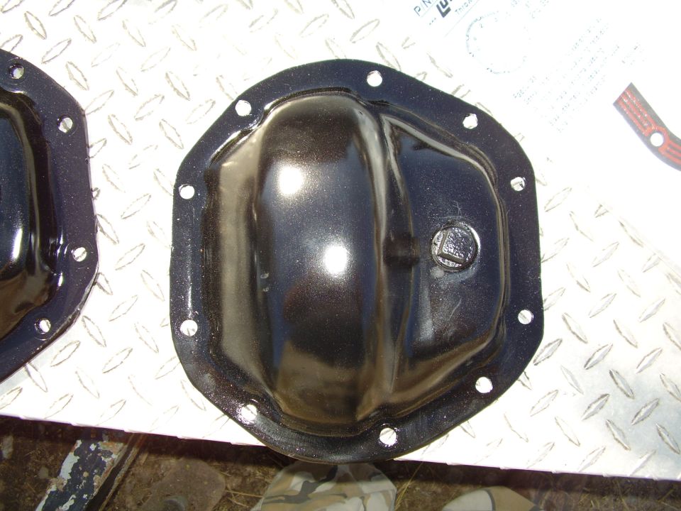 Two black differential covers on a diamond plate surface, one in focus with a bolt head visible