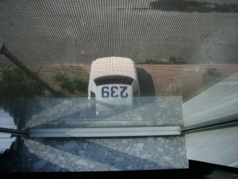 2000 Ford Crown Victoria - A white vehicle's rear is visible, displaying the number 239, viewed through a window screen.