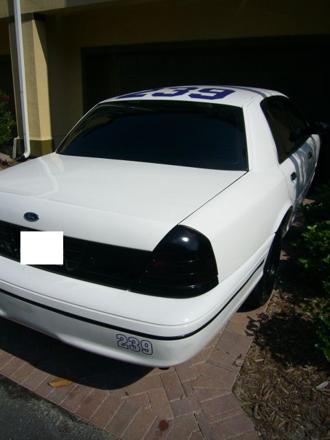 2000 Ford Crown Victoria - A white sedan with blue numbers 239 is parked in front of a garage.