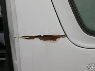 1995 Ford C-350 (Centurion Conversions) - Rust is visible on the side of a white vehicle door, indicating corrosion and damage.