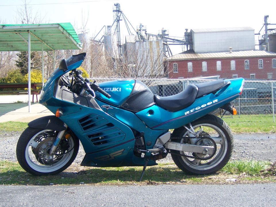 Teal Suzuki sport motorcycle parked outdoors with industrial buildings in the background