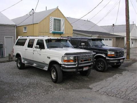 1995 Ford C-350 (Centurion Conversions) - Two Ford C-350 Centurion Conversions SUVs, one white and one black, are parked in front of buildings.