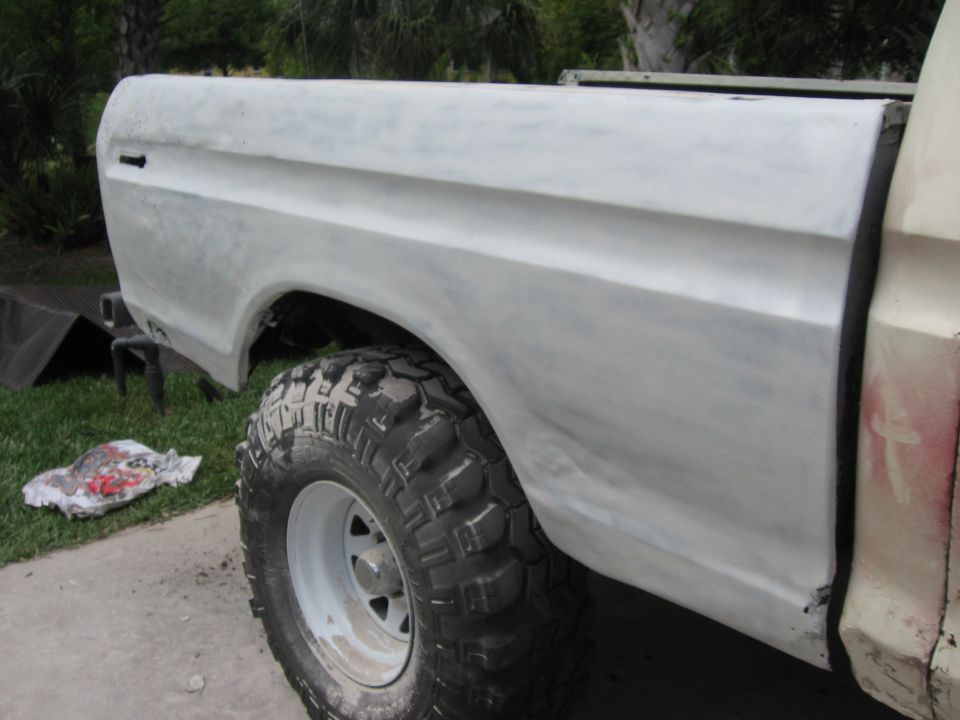 Gray primer Ford F-100 truck bed with large off-road tire visible