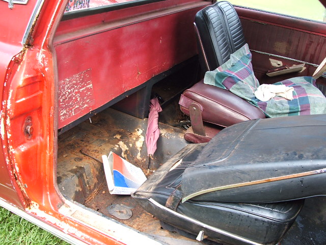 Rusty stripped interior of a red project car with bare floor pans and loose seats
