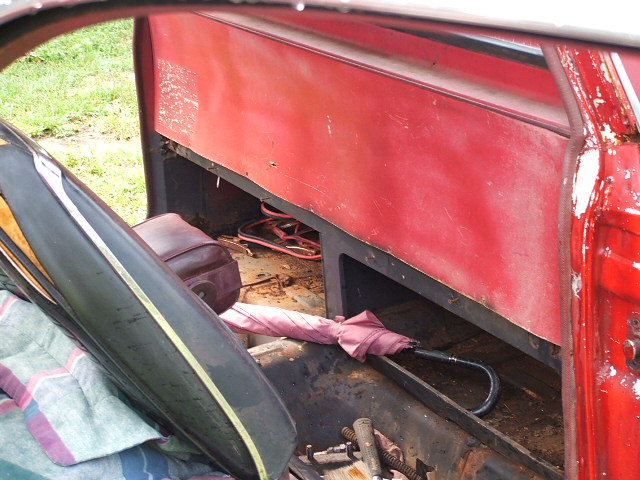Stripped interior of faded red project car with rusty floor pan