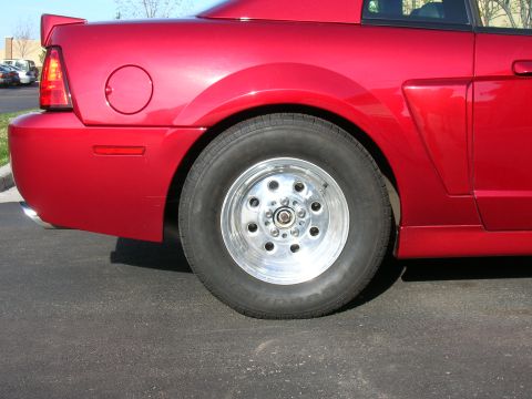 1979 Ford Bronco - Rear quarter panel and wheel of a red car, possibly a Mustang, with drag racing wheels.