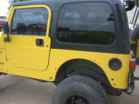 2001 Jeep Wrangler - This yellow Jeep Wrangler features a black hardtop and is viewed from the side, showing its spare tire mounted on the rear.