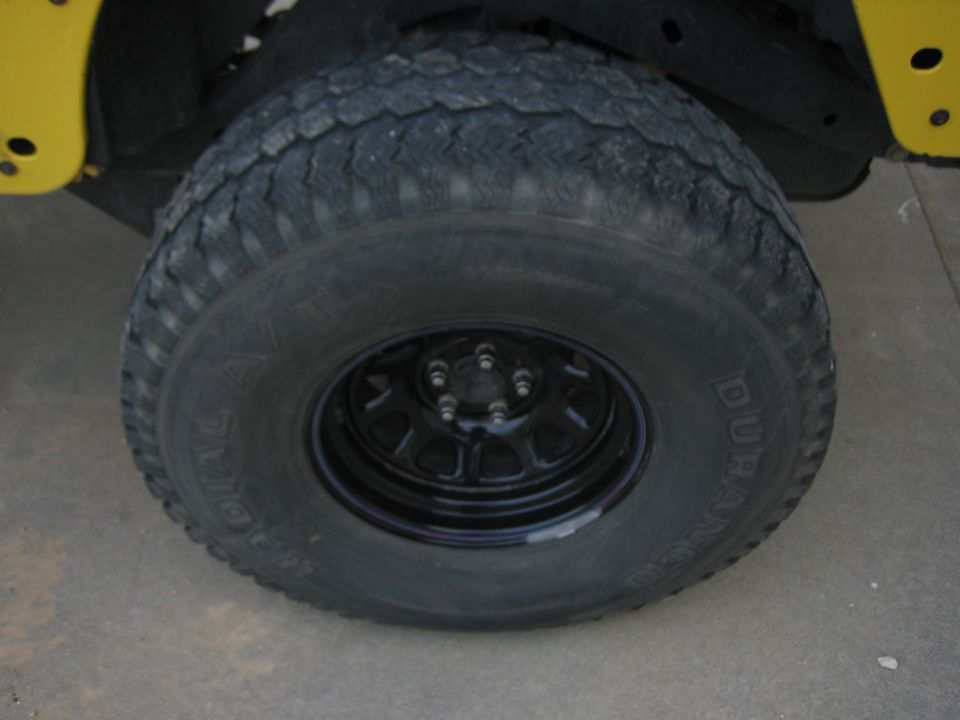 Close-up of a black Jeep Wrangler wheel with a Duratrac tire. Yellow body panel visible