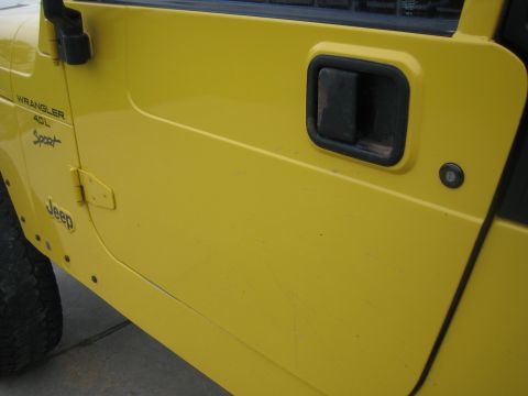 2001 Jeep Wrangler - Close-up of a yellow Jeep Wrangler door, showing the 'Jeep' and 'Wrangler 4.0L Sport' badging.