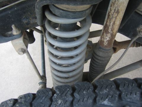 2001 Jeep Wrangler - Close-up view of the front suspension system, including a coil spring and shock absorber, with tire tread in the foreground.