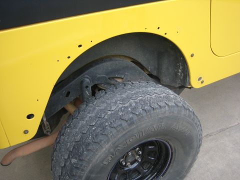 2001 Jeep Wrangler - Close-up of the rear wheel well of a yellow Jeep Wrangler, showing the tire and suspension components.