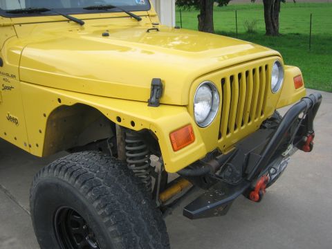 2001 Jeep Wrangler - Front corner view of a yellow Jeep Wrangler with a custom bumper and off-road tires.