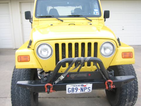 2001 Jeep Wrangler - A yellow Jeep Wrangler is parked in front of a garage door, showing its front grille and bumper.
