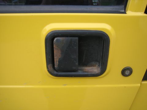 2001 Jeep Wrangler - The exterior door handle of a yellow vehicle shows signs of rust and age.