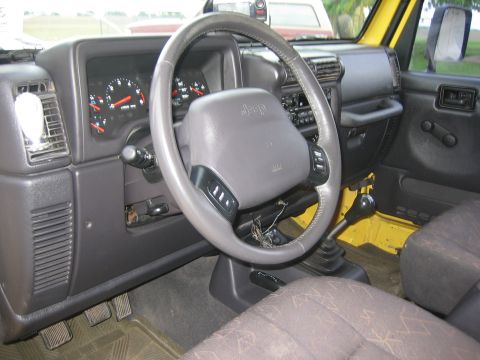 2001 Jeep Wrangler - The interior of a yellow 2001 Jeep Wrangler is visible, with a focus on the dashboard and steering wheel.