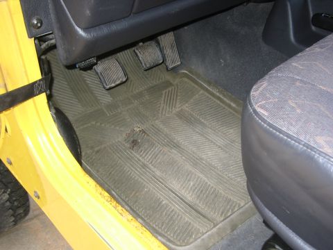 2001 Jeep Wrangler - The driver's side interior of a yellow vehicle, showing the pedals and a rubber floor mat.