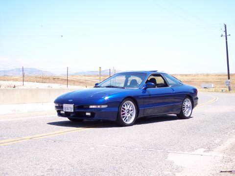 1995 Ford Probe - A blue 1995 Ford Probe is captured in a three-quarter front view while driving on a paved road under a clear sky.