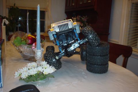 2000 Ford Crown Victoria - A remote-controlled Jeep Wrangler toy is positioned on a table, with a stack of tires nearby.