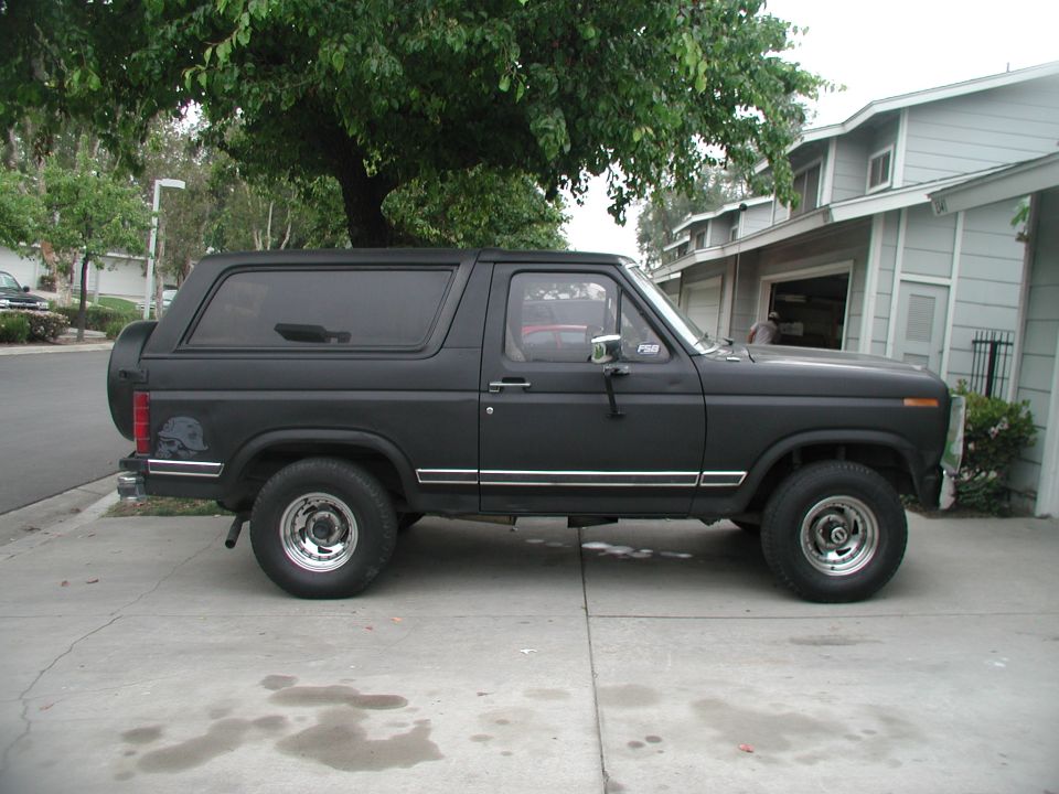 Black Ford full-size Bronco with camper shell parked curbside, profile view