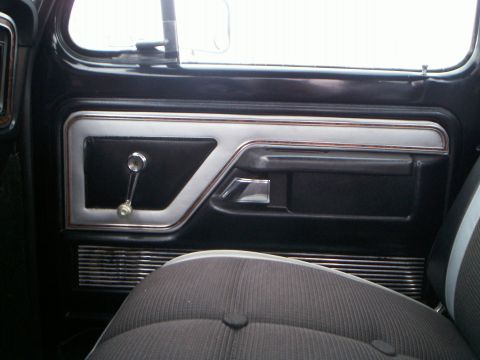 1979 Ford F-250 - The interior door panel of a 1979 Ford F-250 features a black and chrome design with a manual window crank and textured seat fabric.