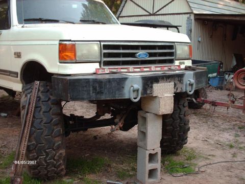 1990 Ford F-150 - Front view of a lifted 1990 Ford F-150 truck, undergoing modifications with support blocks and a jack.