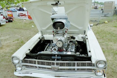 1976 Ford Ranchero - A white 1966 Ford Falcon features a prominent supercharger and scoop under its open hood at an outdoor event.