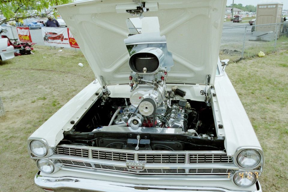 Blown supercharged V8 in engine bay of white 1960s Ford XL at outdoor car show