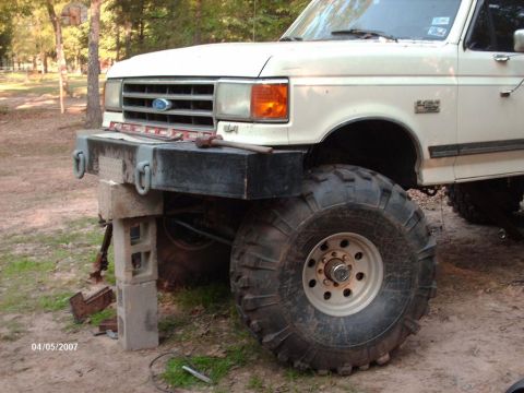 1990 Ford F-150 - A white Ford F-Series truck with oversized tires and a custom bumper is elevated on cinder blocks.