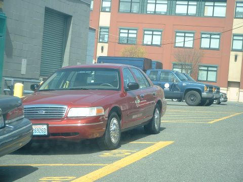 2000 Ford Crown Victoria - A red 2000 Ford Crown Victoria is parked in a lot, with other vehicles visible behind it.