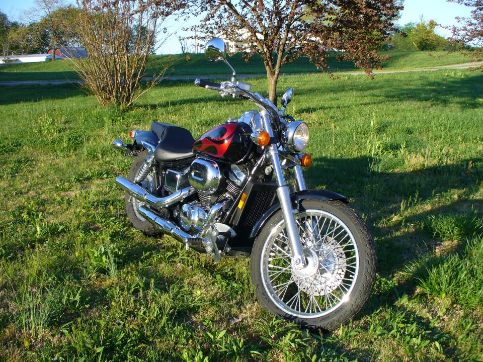 Cruiser motorcycle with red flame tank parked on grass, 3/4 front view