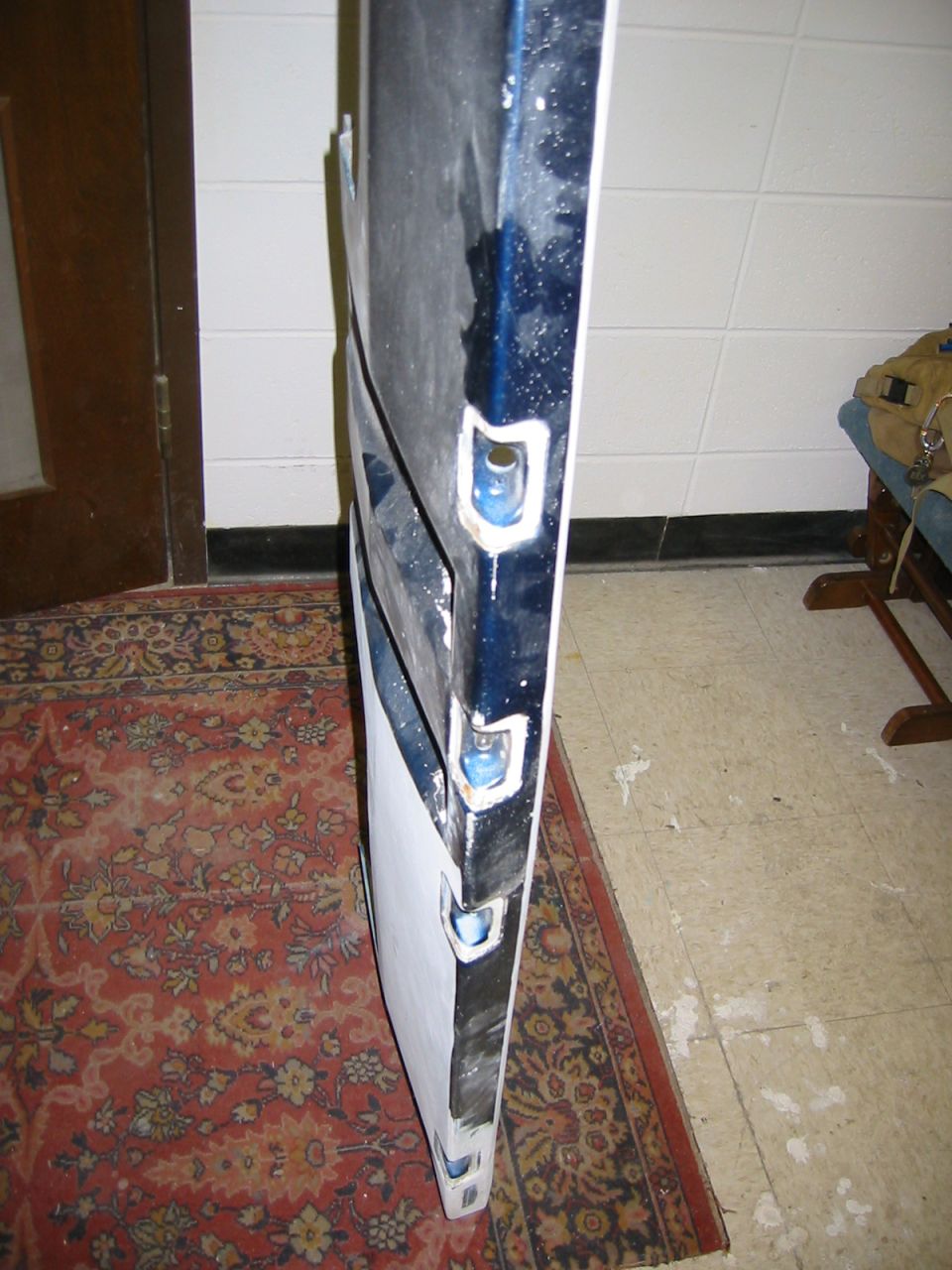 Blue car door with white primer on the edge, showing mounting holes