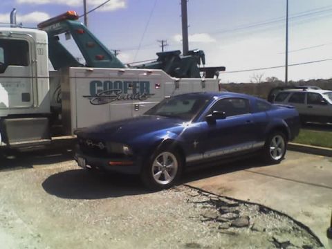 1992 Ford Bronco - A blue Ford Mustang is parked next to a tow truck, with a white SUV visible in the background.