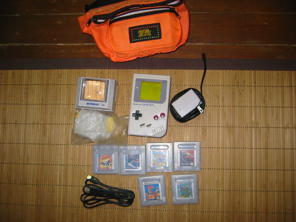Nintendo Game Boy, games, charger, and orange fanny pack on a bamboo mat