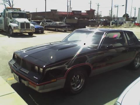 1992 Ford Bronco - A black coupe with red pinstripes is parked on asphalt, with a tow truck visible in the background.