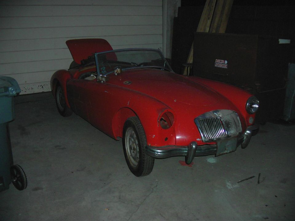 Red MG A roadster in garage, 3q-front view, hood up, top down