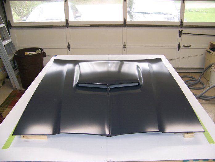 Black cowl-induction hood with center scoop laid on supports in a garage