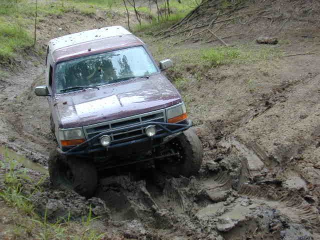 Burgundy Ford Bronco with brush guard driving through a deep mud rut