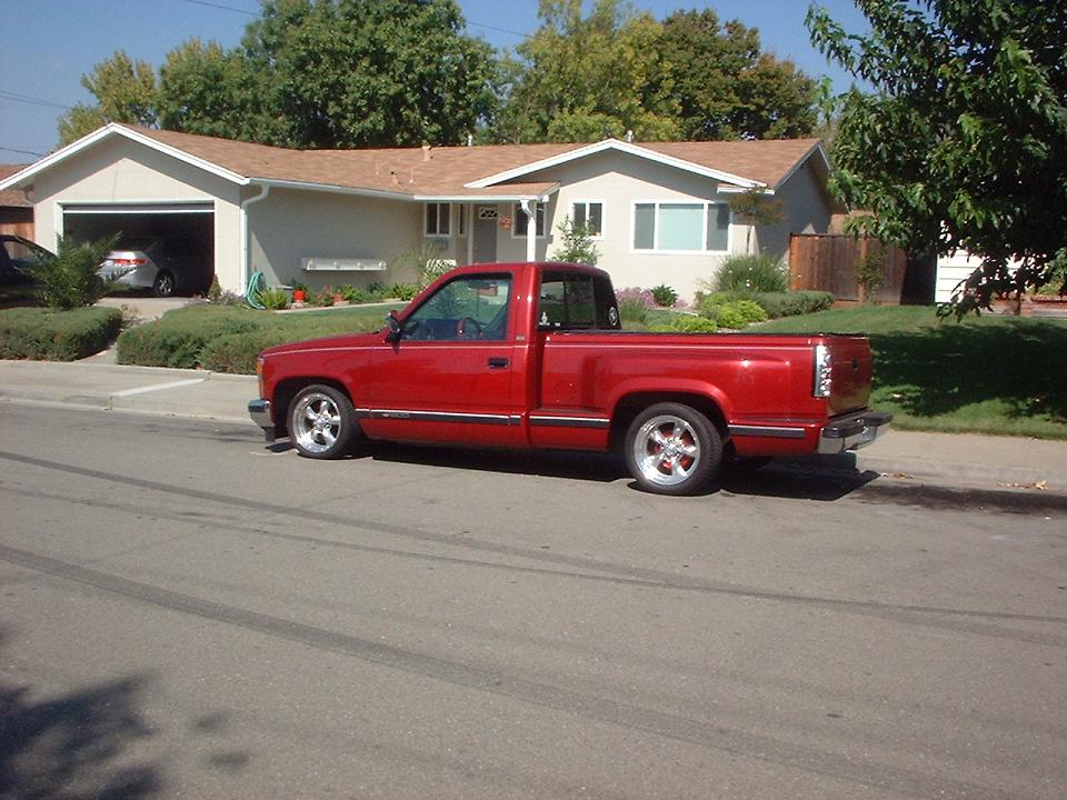 Red pickup truck, lowered, with chrome wheels, parked on street