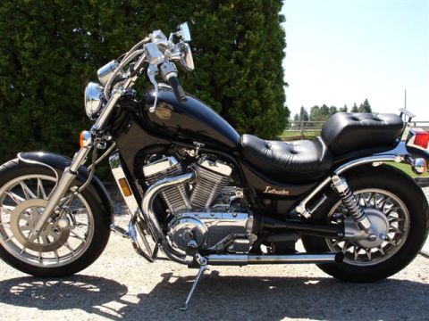 1979 Ford F-150 - Left-side profile of a black Suzuki Intruder cruiser motorcycle parked on its sidestand on a gravel driveway, with gold 'Intruder' script o…
