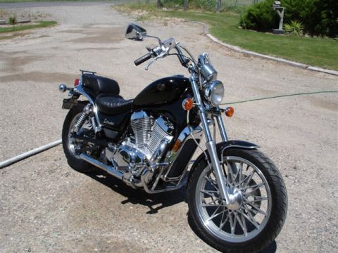 1979 Ford F-150 - Three-quarter front view of a black Suzuki Intruder cruiser motorcycle parked on a gravel driveway beside a grass lawn and hedge. The bike…