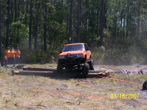 1989 Ford Bronco - An orange off-road SUV navigates an obstacle course in a wooded area.